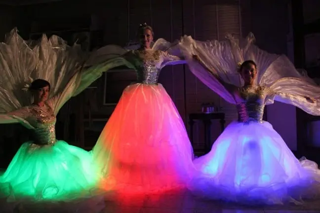 LED dancers in glowing ball gowns lit green, red and violet, with white wings