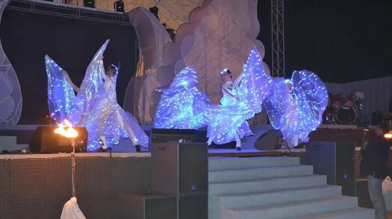 LED dancers with glowing wings performing on an outdoor stage at night