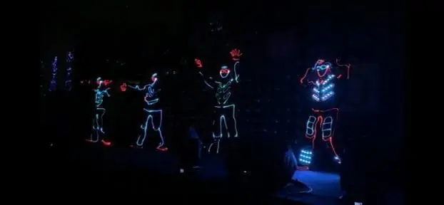 LED tron dancers and an LED robot performing together on a dark stage