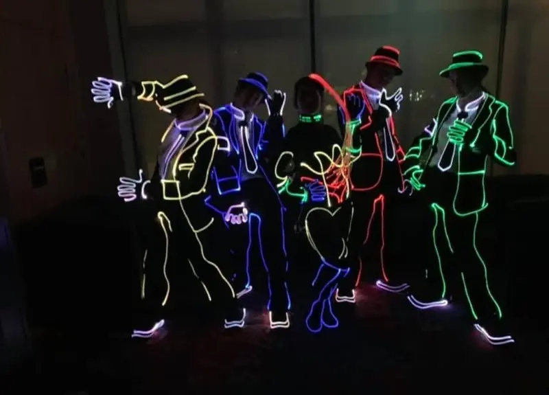Tron dancers in glowing light-strip suits and hats posing together in a dark room